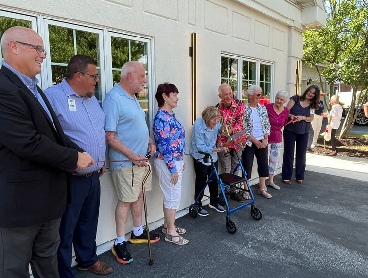 A small group of senior citizens in a line, as one cuts a ribbon